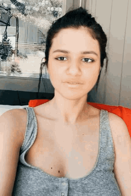 a woman in a grey tank top is sitting in front of a window looking at the camera