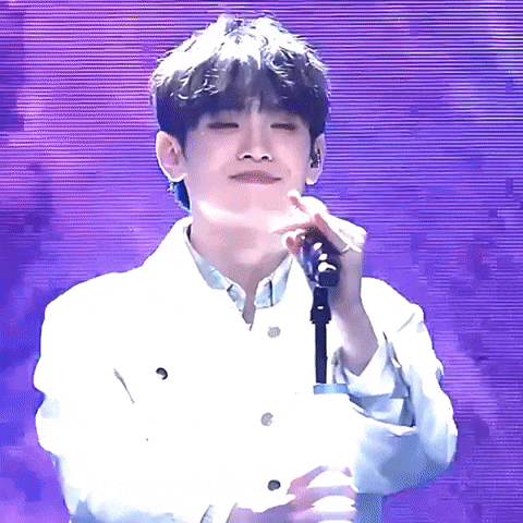 a young man in a white jacket is singing into a microphone on a stage .