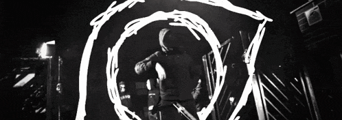 a black and white photo of a person in a hooded jacket standing in a dark tunnel .
