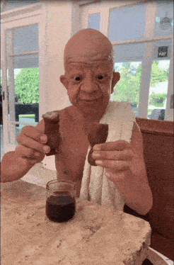 a shirtless bald man is sitting at a table holding a piece of food