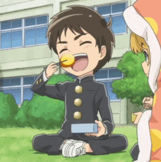 a boy in a school uniform is sitting on the grass eating a cookie .