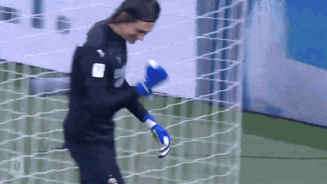 a soccer goalie wearing blue gloves stands in front of a soccer net