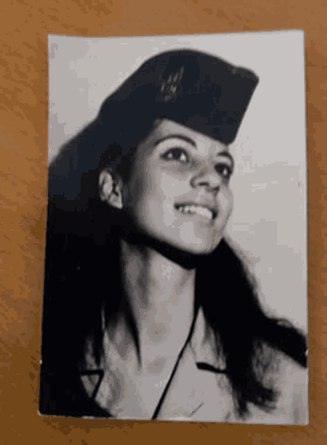 a black and white photo of a woman wearing a hat is on a wooden table .