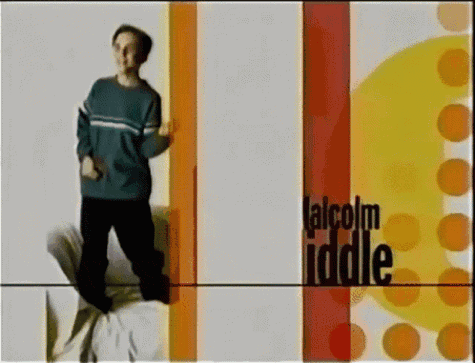 a man in a blue sweater is standing in front of a sign that says " talcolm iddle "