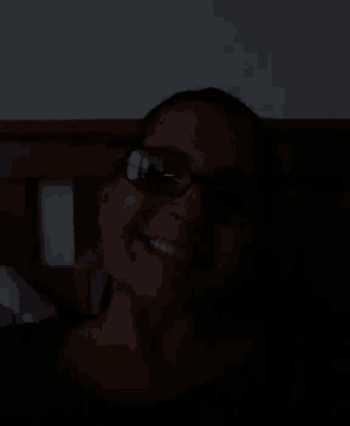 a woman wearing glasses and smiling in the dark