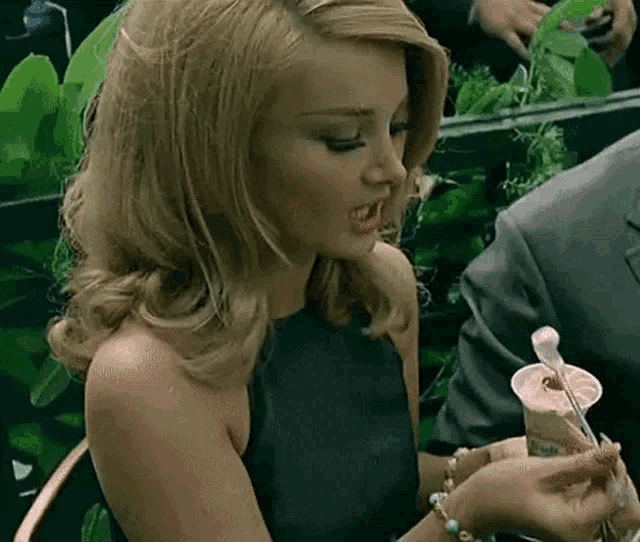 a woman in a black dress is holding a cup of ice cream with a spoon in it .