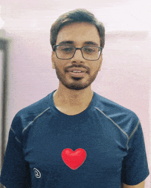 a man wearing glasses and a blue shirt has a red heart on his shirt
