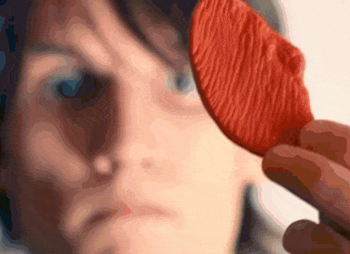 a close up of a person holding a red item in front of their face
