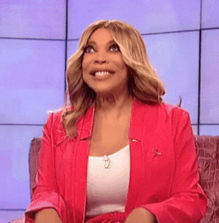 a woman in a red jacket and white tank top is sitting on a couch and smiling .