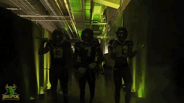 three football players for the bullpen walk through a tunnel