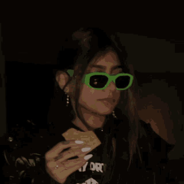 a woman wearing green sunglasses is smiling and holding a piece of s'mores