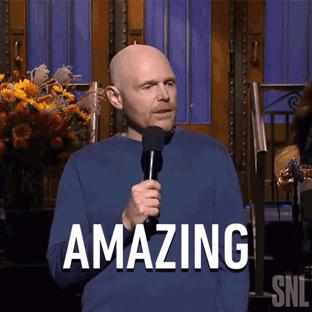 a bald man is holding a microphone and the word amazing is on the screen behind him