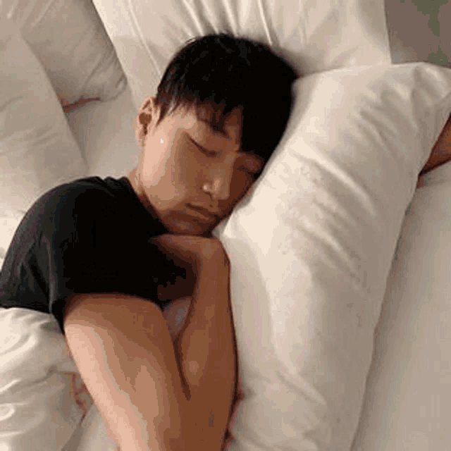 a young man is sleeping on a bed with a pillow around his neck .