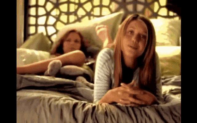 two girls are laying on a bed with their feet up .