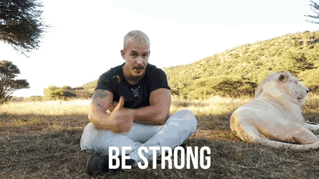 a man sits in the grass next to a lion that says be strong on the bottom