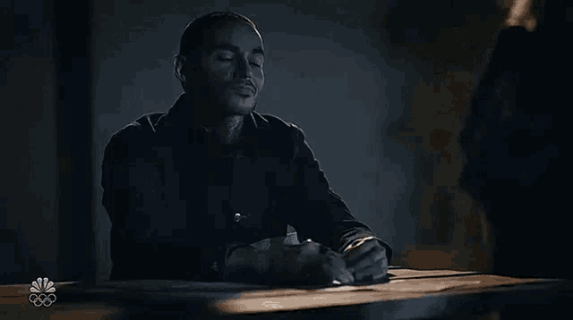 a man is sitting at a table with his eyes closed and a cigarette in his mouth .