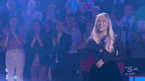 a woman stands in front of a crowd that is clapping and has the number 5 on her shirt