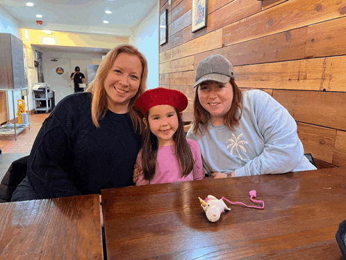 a little girl wearing a red beret sits between two women