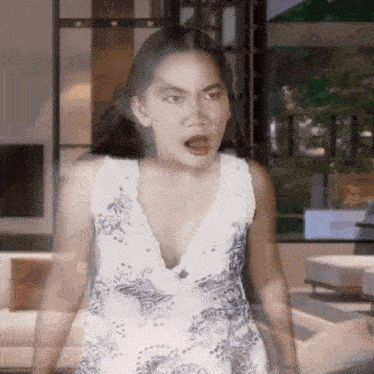 a woman in a white dress is standing in front of a window and making a funny face