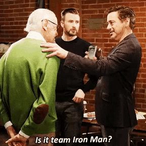 a man in a green sweater talks to two other men with the caption is it team iron man ?