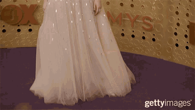 a woman in a white dress is standing in front of a wall that says fox mys