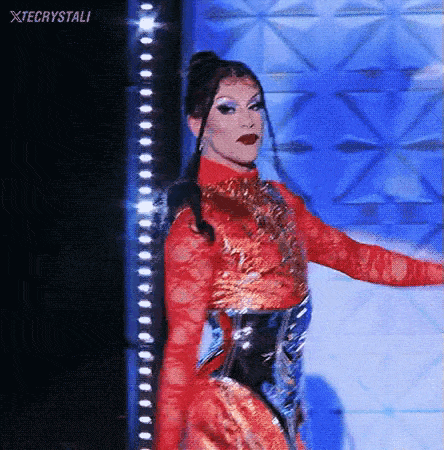 a drag queen is standing on a stage wearing a red and gold dress .