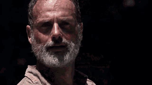 a man with a beard is pointing a gun at the camera with blood on his hand .