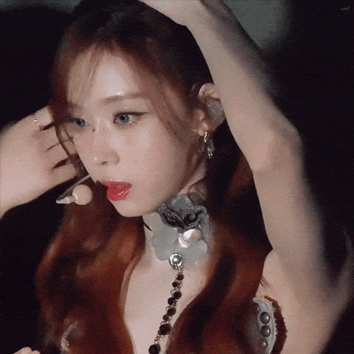 a woman with red hair is wearing a choker and earrings and adjusting her hair