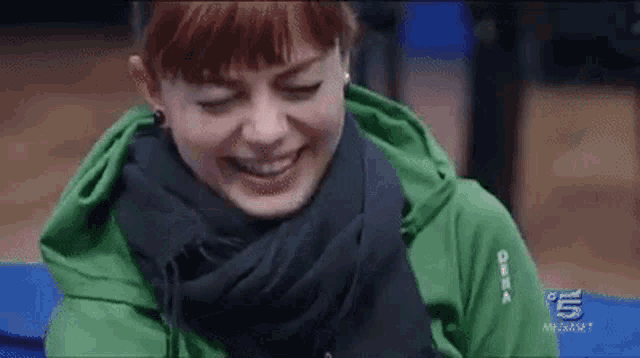 a woman wearing a green hoodie and a black scarf is laughing .