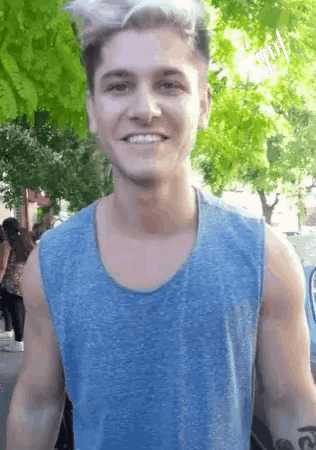 a man in a blue tank top is smiling in front of trees .