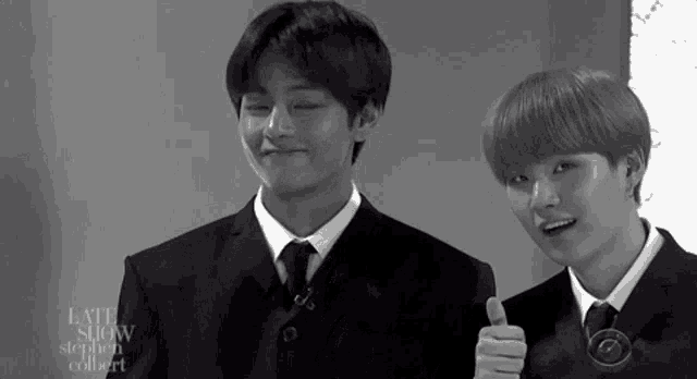 two young men in suits and ties are standing next to each other and giving a thumbs up .