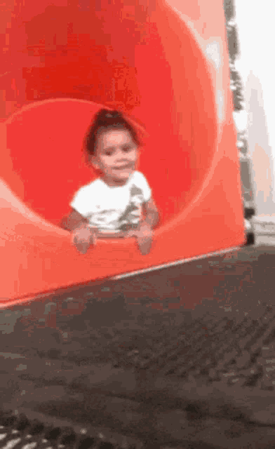a little girl is sitting on a red slide .