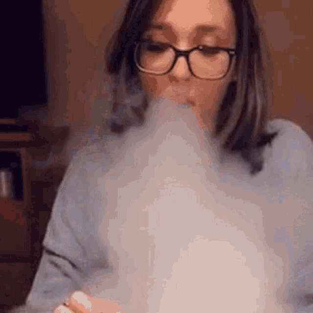 a woman in glasses is blowing smoke out of her mouth .