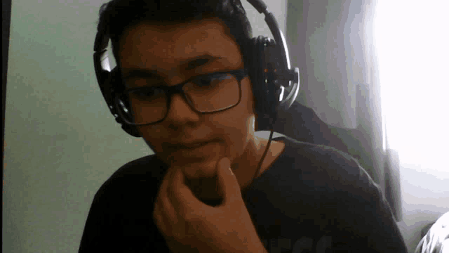 a boy wearing glasses and headphones has his hand on his face