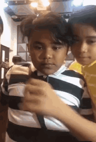 a boy in a black and white striped shirt is being held by another boy in a yellow shirt