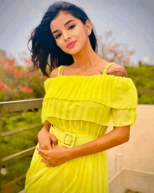 a woman in a bright yellow off the shoulder dress is standing on a balcony