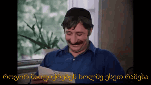 a man with a mustache is smiling while holding a piece of paper in front of a window