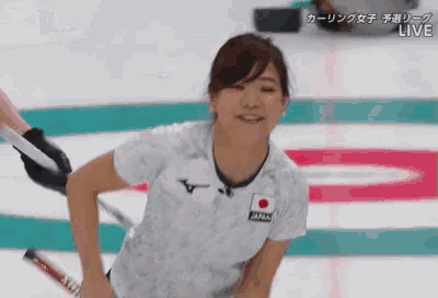 a woman in a white shirt with a red circle on it is playing curling .