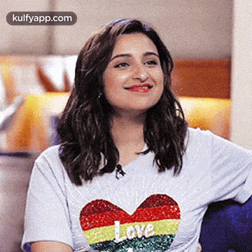 a woman wearing a white t-shirt with a heart on it is smiling and sitting on a couch .