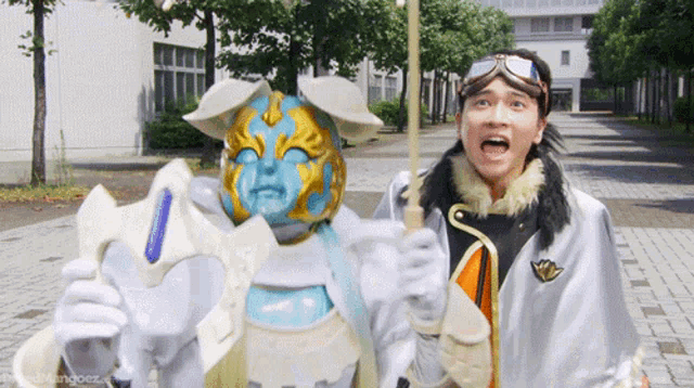 a man is standing next to a blue and gold masked monster