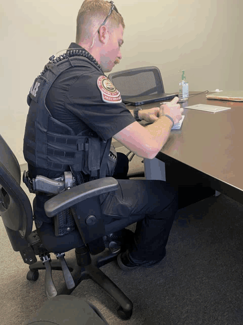 a police officer sits at a table writing on a piece of paper with a patch that says police