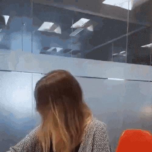 a woman in a grey sweater is sitting at a desk in front of a glass wall .