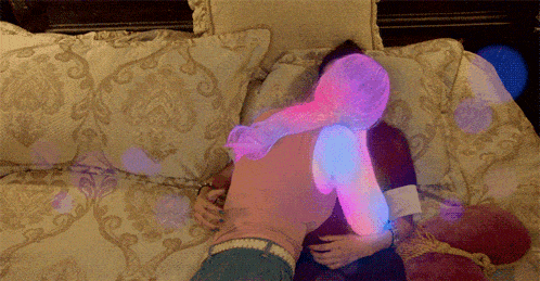 a woman in a pink shirt is laying on a bed hugging another woman