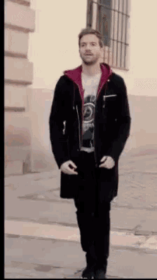 a man wearing a black coat and a red hoodie is walking down a street