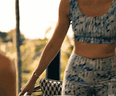 a woman in a crop top and pants is standing next to a man in a chair .