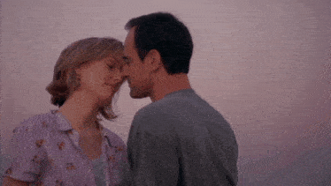 a man and a woman kissing with a pink sky in the background
