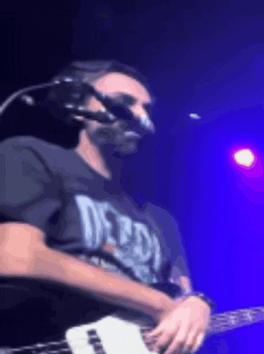 a man wearing a t-shirt that says deadly is playing a guitar on stage