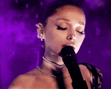 a woman singing into a microphone with purple background