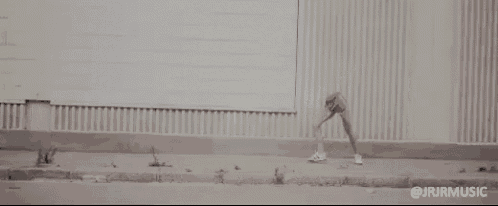 a black and white photo of a person standing on a sidewalk in front of a wall .