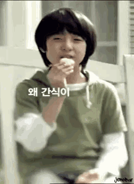 a young boy is eating a piece of food with chopsticks while wearing a green shirt .